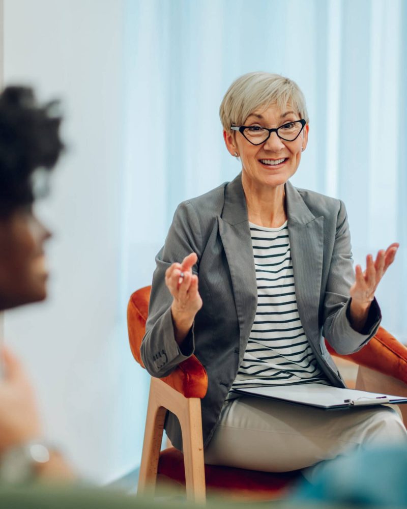 Portrait of a smiling and attentive mature female doctor is listening to her clients mental and marriage problems in her office while taking notes. Psychotherapy consultation. Copy space.